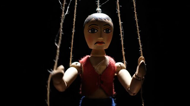 Wooden Puppet Suspended by Strings in Dark Theatrical Setting.