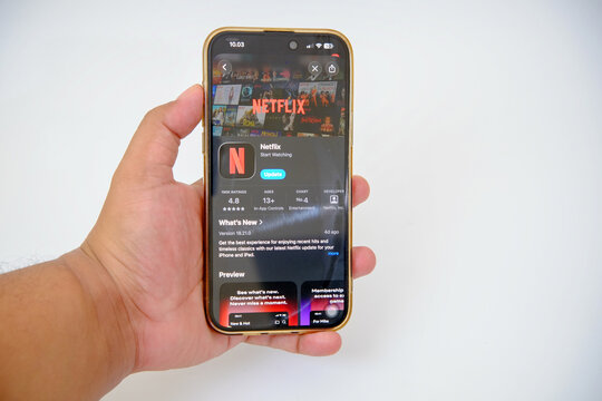 Phone User Holding a Modern Smartphone Showcasing the Netflix Streaming Service Application Details on the App Store Ready for an Update with Ratings and Preview Information