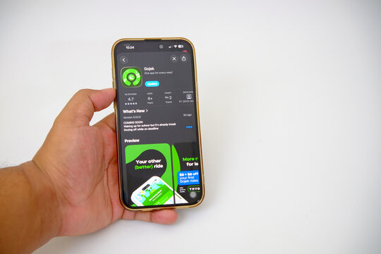 Smartphone Displaying the Gojek Application Update Page in an App Store Showcasing Its Features and Ratings on a Dark Interface Held by a Hand Against a White Background