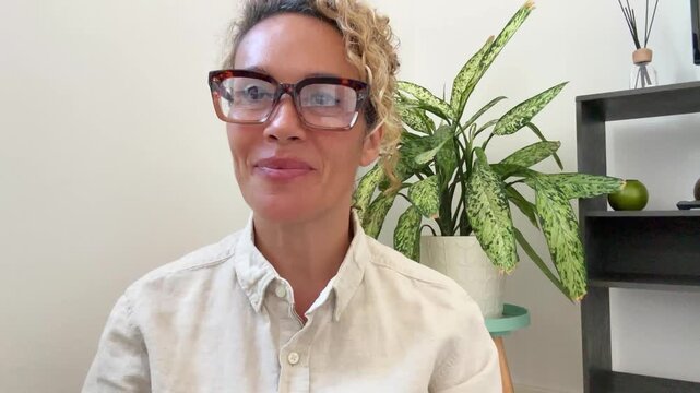 Confident middle-aged woman smiling and gesturing during a professional video call at home. Caucasian adult managing remote work, leading team discussion and business tasks efficiently.