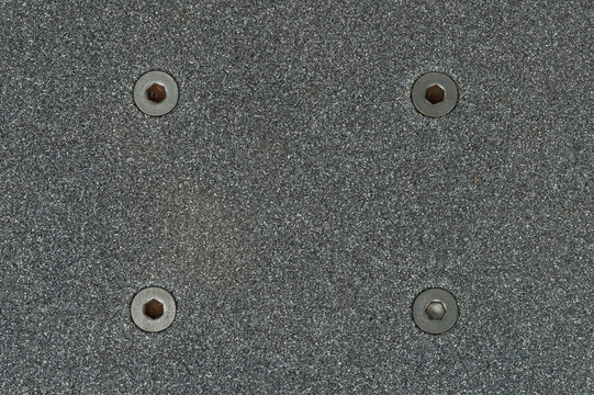 Close view of a skateboard deck with grip tape and screws