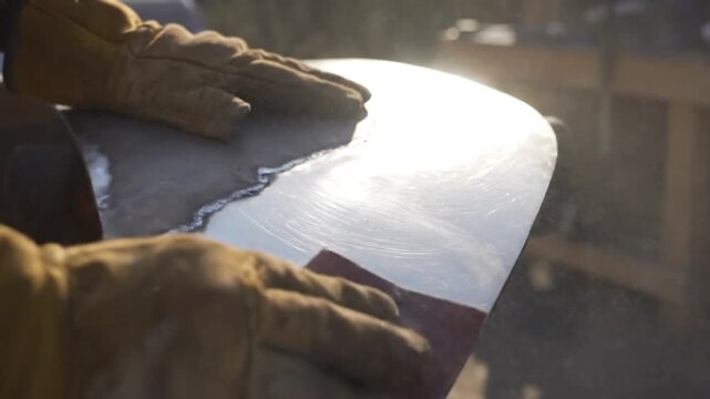 Close up view of worker wearing leather gloves carefully sanding the metal surface of a shovel blade restoration project.