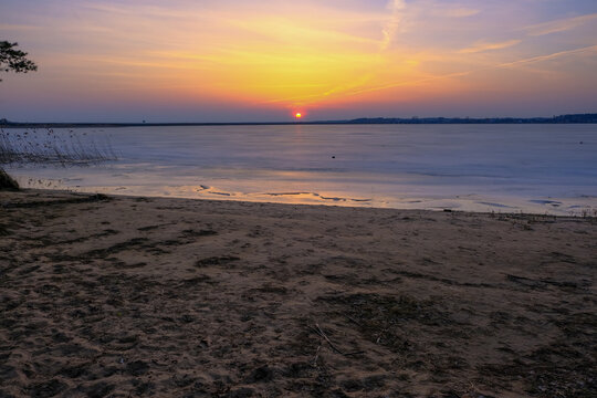Sunset over frozen lakeshore near Minsk with reeds and sand