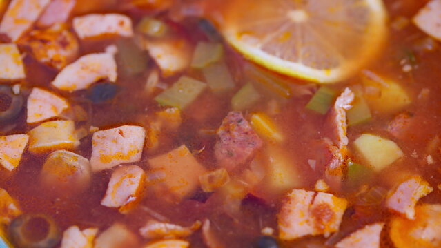 Rich tomato broth with smoked ingredients, Hearty smoked meat and vegetable stew with vibrant colors, Flavorful smoky solyanka soup featuring lemon slice and rustic presentation