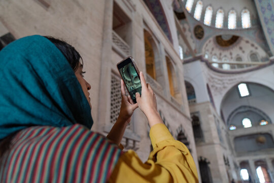 Young female tourist visiting mosque and taking photos and videos with her smart phone