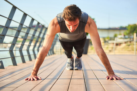 Young man performing push-ups on bridge pavement