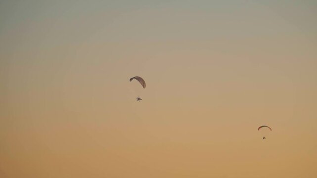Silhouette shot of two Parachutes against the orange sky during the sunset as seen from Rann of Kutch during winter season at Dhordo in Kutch, Gujarat, India. People enjoying Paragliding activity.