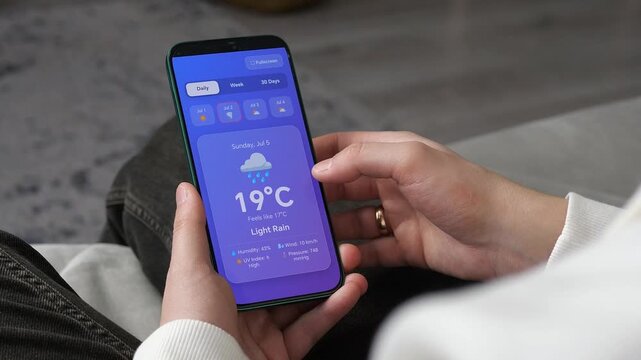 Close-up of hands using a weather forecast app on a smartphone. Person checking daily temperature and conditions. Concept of mobile technology, travel planning, and daily lifestyle routine.