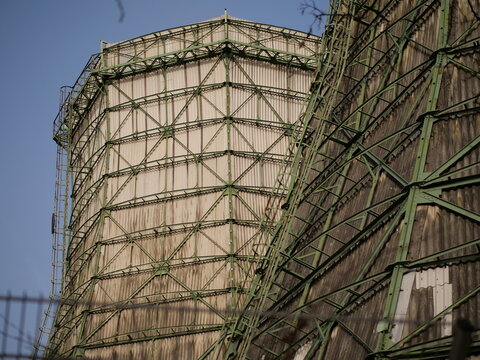 Industrial cooling towers with green steel framework and weathered wood paneling under a blue sky. Detailed view of massive power plant infrastructure, engineering architecture, and heavy industry fac