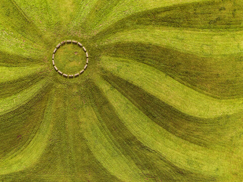 An aerial shot of wooden benches in a circle and grass mowed to resemble the rays of the sun
