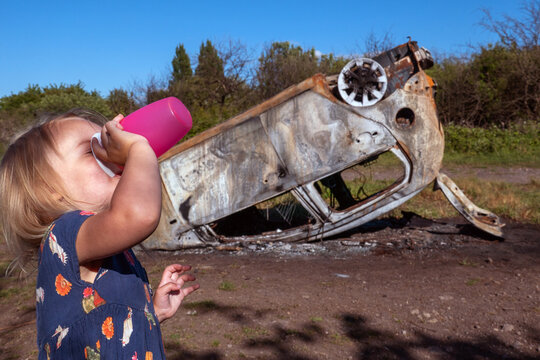 A girl drinks from her bottle of water in front of a burnt out car