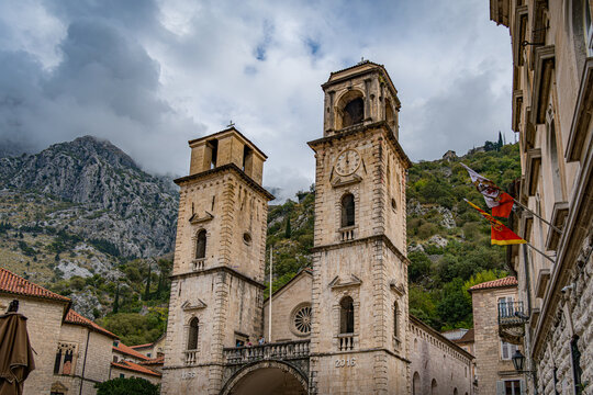 Historic towers stand tall in Kotor, Montenegro under a cloudy sky surrounded by mountains in early evening light