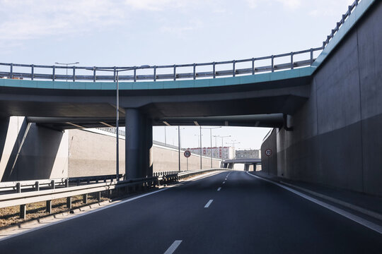 Empty highway road passing under modern concrete overpass and bridge structure. Urban transport infrastructure with multilane asphalt roadway, barriers and flyover viaduct in daylight travel concept.