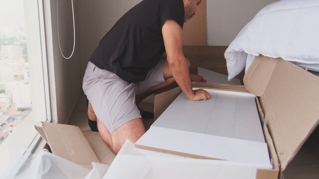 Young man unpacking a cardboard box and assembling a new piece of furniture in his apartment