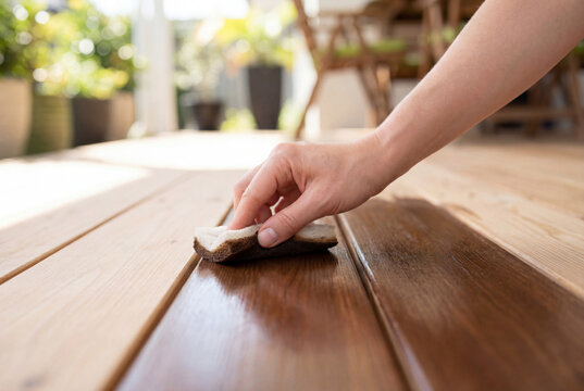 Hand applying dark brown wood stain protector to a new outdoor larch wood deck