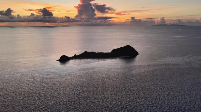 A serene sunrise silhouettes a small island in the Vatu-i-ra seascape in Fiji. This area is a marine protected area known for its high biodiversity and is a destination for divers and snorkelers.