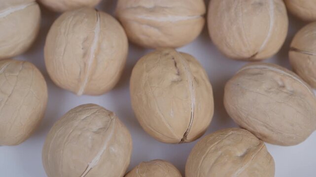 Shells arranged on white background. Tightly packed walnuts with textured shells displayed. Closeup of arranged walnuts with ridged shells and cracks on neutral background