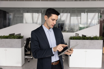 Fototapeta premium Focused young adult Latin businessman corporate professional executive reviewing data on digital tablet using app to analyze information reading marketing research online in modern office workspace
