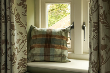 Plaid cushion resting on a window seat, framed by patterned curtains, creating a cozy and comfortable home interior