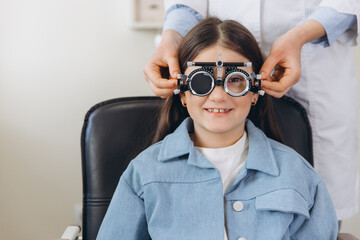 Young girl smiling during pediatric eye exam, optometrist adjusting trial frame for vision testing © anatoliycherkas