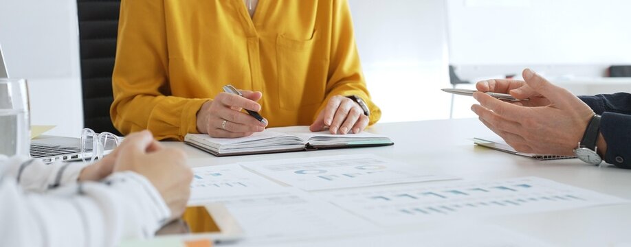Business team collaborating and analyzing financial data while taking notes during a corporate meeting in a modern office, highlighting teamwork and strategic planning