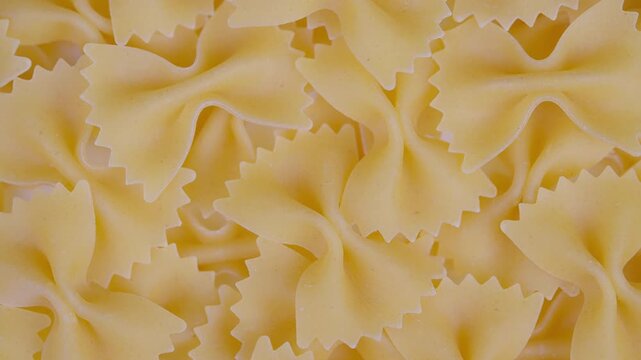 Closeup bowshaped pasta pile showcasing raw farfalle texture warm golden tones overlapping pieces form repeating pattern ideal for food packaging backgrounds recipe visuals