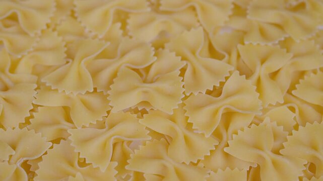 Pasta with textures. Golden bow pasta closeup shot. Detail of dry bowshaped pasta under warm light. Close view of farfalle pasta revealing serrated edges and texture details