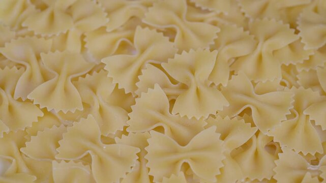Bowshaped pasta with warm lighting. An intimate perspective of mound of dry farfalle pasta featuring soft warm illumination and pale yellow tones in culinary setting