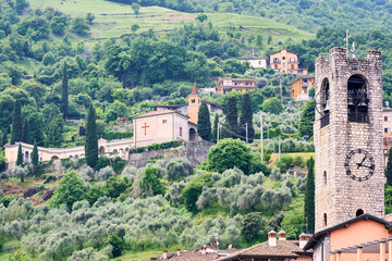 Fototapeta premium Historic Torre bell tower and the Chiesa di San Pietro overlooking the green hillside of Tavernola Bergamasca at Lake Iseo in Lombardy, Italy