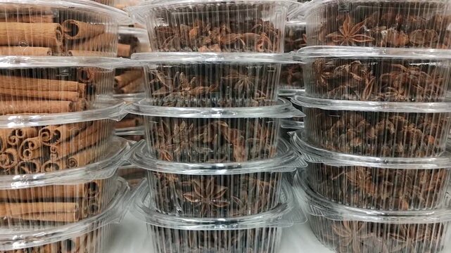 Piles of star anise and cinnamon sticks packed in clear plastic containers on market shelf. Large assortment of aromatic spices in grocery store. Boxes with fragrant badian and cinnamon quills 