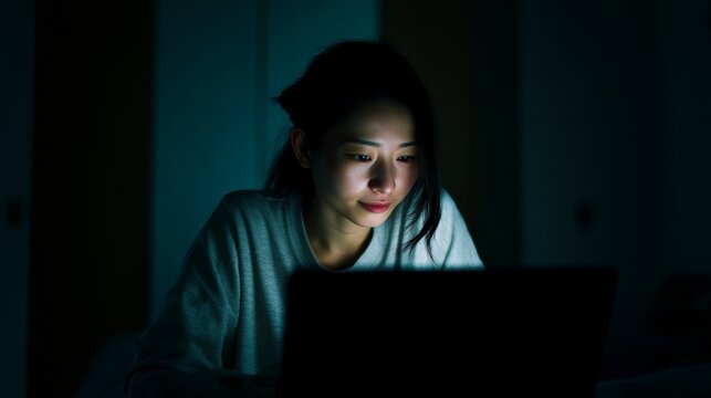 Woman working late at night on her computer in a room with a dim light, showing her focus and dedication to her tasks.