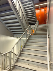 Staircase leading to an orange door in a modern building with gray metal railings and steps during...