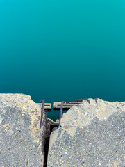 Fototapeta premium View of a cracked pier with visible metal reinforcements near a turquoise blue body of water on a sunny day