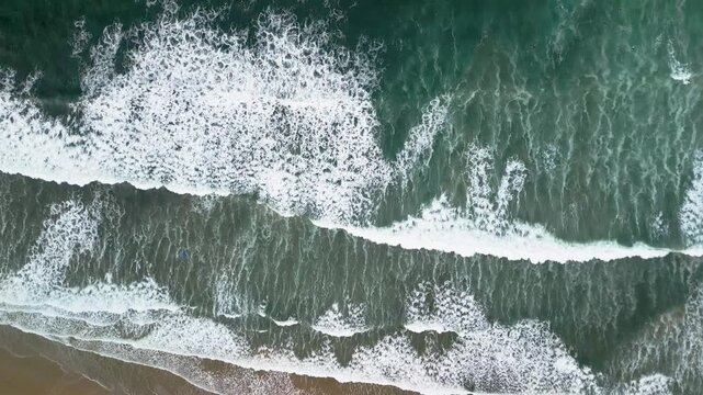 Top down aerial view of blue ocean waves crashing into rocky shore, beautiful white sea foam textures on dark water, Atlantic coast of Spain, 4K drone.
