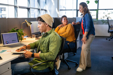 Diverse coworkers collaborating in open-plan office around laptop and printed charts, using tablet