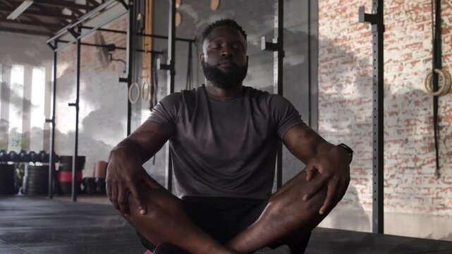 Male fitness trainer ending meditation, moving hands to knees on pink mat for cooldown