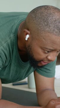 Vertical video: Man in green tee holding forearm plank in bedroom after cue, with earbud dark mat