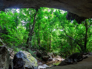 Tham Sumano Cave entrance with lush greenery and rocks. Tropical forest surrounds the cave. Thailand's natural landmark in vibrant outdoor scenery.
