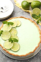 Tasty lime pie with fruit slices and mint leaves on grey textured table, closeup © New Africa