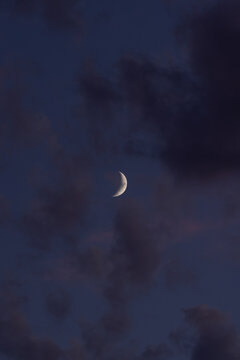 Crescent moon glows softly through deep twilight clouds. Dark, textured clouds drift around the serene lunar curve. Night sky feels calm, quiet, and mysterious. Ideal for tranquil scenes, romance