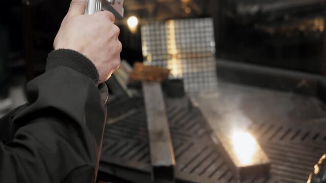 Worker using handheld laser cleaning machine to remove rust and contamination from metal surface during industrial maintenance process in factory.