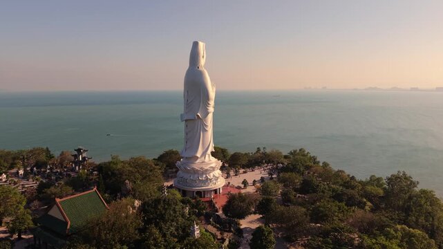 White Guanyin Statue By Turquoise Sea Near Da Nang, Clear Midday Light, Tranquil Waters And Lush Temple Gardens, Aerial Reveal Of Shoreline, Lotus Pedestal And Peaceful Pilgrimage Setting.