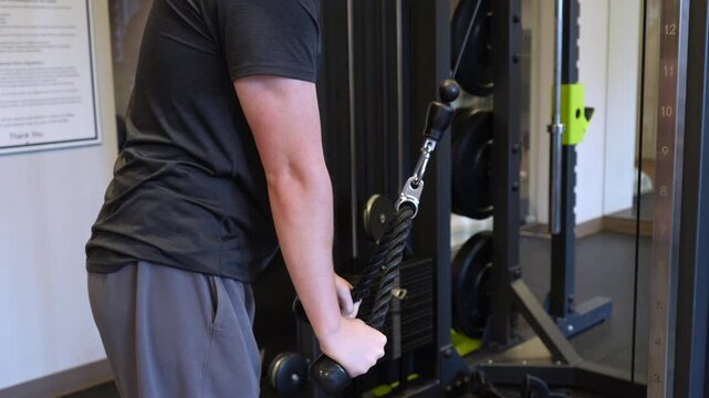 Side view of a man performing cable rope pulldowns in a gym. The mood is determined and focused. This clip is ideal for fitness, health, and workout content