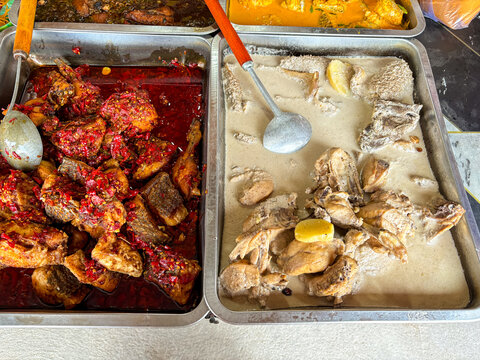 Traditional Indonesian Padang cuisine, chicken or ayam goreng balado with spicy red chili sauce and gulai ayam cooked in rich coconut milk. Served in stainless trays at local food vendor. closeup