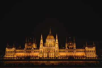 Obraz premium The illuminated Hungarian Parliament Building stands as a majestic landmark over the Danube river at night, reflecting the historic architecture of Budapest, Hungary’s capital city in Europe