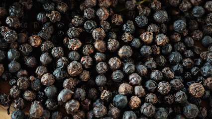 Obraz premium Closeup of black peppercorns on a wooden plate.
