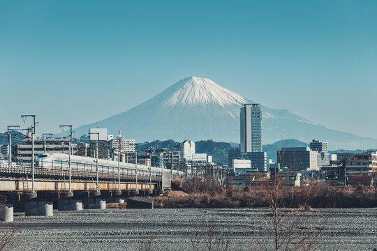 安倍川に架かる鉄橋を走るJR東海道新幹線の背後には静岡市の都市景観と富士山が見える