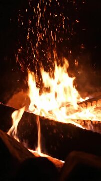 Flames rise high as logs burn in a campfire during a cool night in the woods