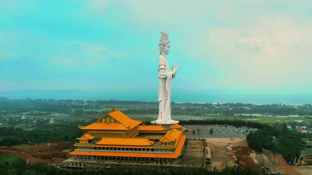 4K drone orbit of the hilltop Minh Duc Pagoda and giant statue, overlooking the residential town and coastal area of Quang Ngai in early morning mist.