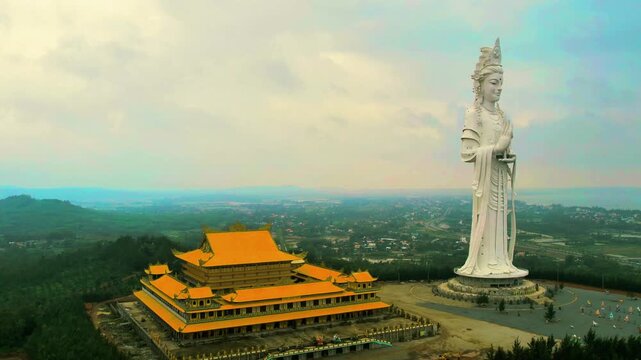 4K aerial orbit in front of the grand main hall of Minh Duc Pagoda, featuring the towering Avalokitesvara Bodhisattva statue sừng sững.